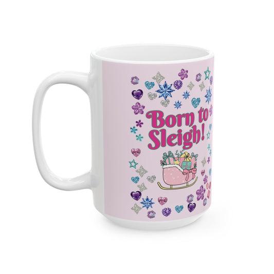 A white festive ceramic mug with a light pink printed wrap design featuring the text 'Born to Sleigh!' in pink, surrounded by colorful glitter-style hearts, snowflakes, stars, and a small sleigh carrying presents.