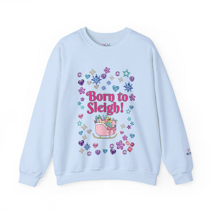 A light blue crewneck sweatshirt featuring a colorful 'Born to Sleigh!' graphic on the front, surrounded by glittery hearts, stars, and snowflakes, with a pink sleigh illustration below.