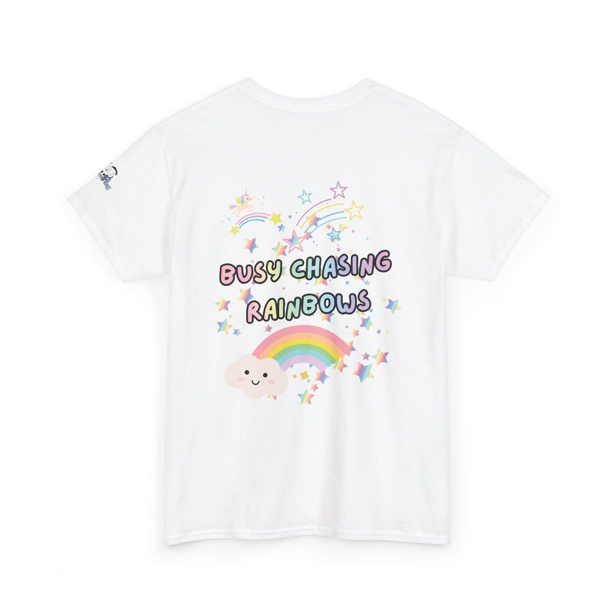 A white short-sleeve t-shirt with a colorful graphic on the front featuring the text 'BUSY CHASING RAINBOWS' in pastel bubble letters, surrounded by a smiling cartoon cloud, a rainbow, and stars.