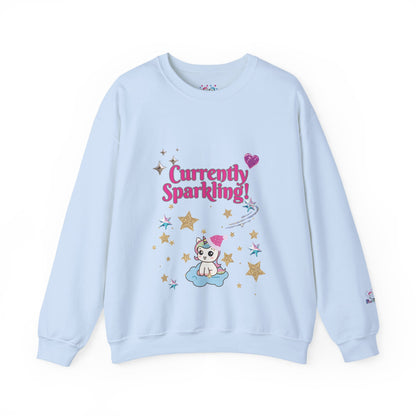 A light blue Christmas crewneck sweatshirt featuring a colorful graphic on the front with the text 'Currently Sparkling!' in pink, a cute cartoon cat on a cloud, and gold stars. 