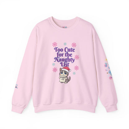 A light pink crewneck sweatshirt featuring a cute cartoon cat wearing a Santa hat and holding a sign that reads 'Cute List' surrounded by purple text that says 'Too Cute for the Naughty List' and colorful snowflake graphics.